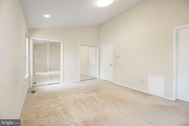 unfurnished bedroom with carpet, visible vents, baseboards, vaulted ceiling, and multiple closets