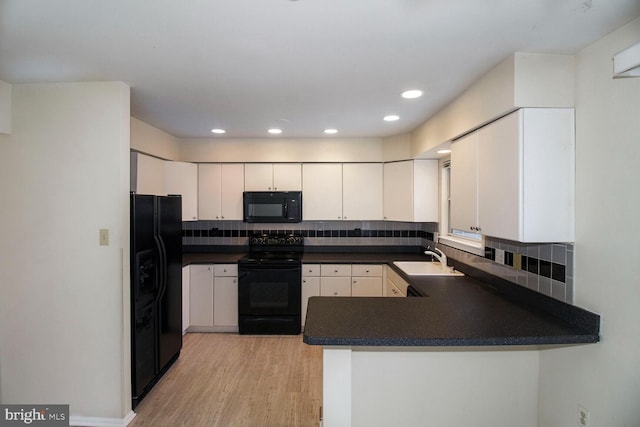 kitchen with dark countertops, a peninsula, light wood-style floors, black appliances, and a sink