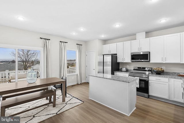 kitchen with white cabinets, appliances with stainless steel finishes, a kitchen island, and light wood-type flooring