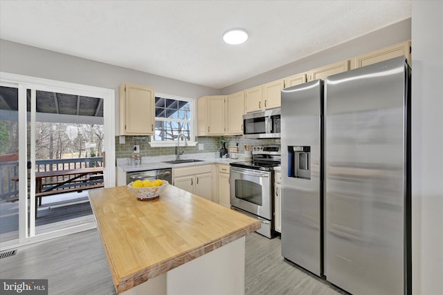 kitchen featuring backsplash, light wood-type flooring, appliances with stainless steel finishes, cream cabinets, and a sink