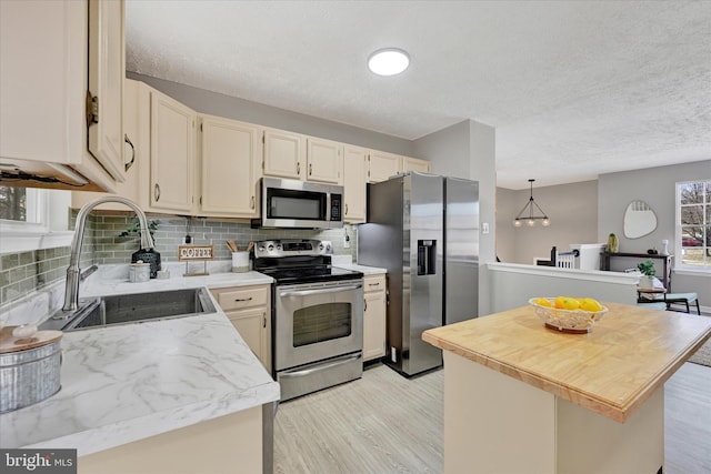 kitchen featuring light wood finished floors, a sink, stainless steel appliances, a textured ceiling, and tasteful backsplash