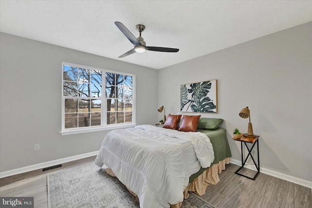 bedroom featuring visible vents, ceiling fan, baseboards, and wood finished floors