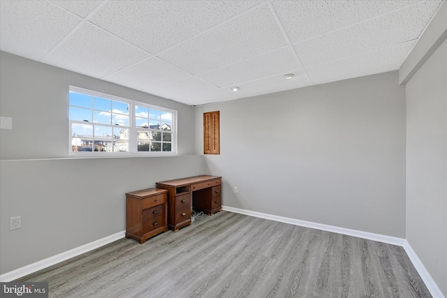 unfurnished office featuring a paneled ceiling, baseboards, and light wood-style floors