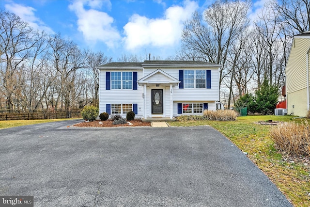 bi-level home featuring aphalt driveway, central AC unit, a front lawn, and fence