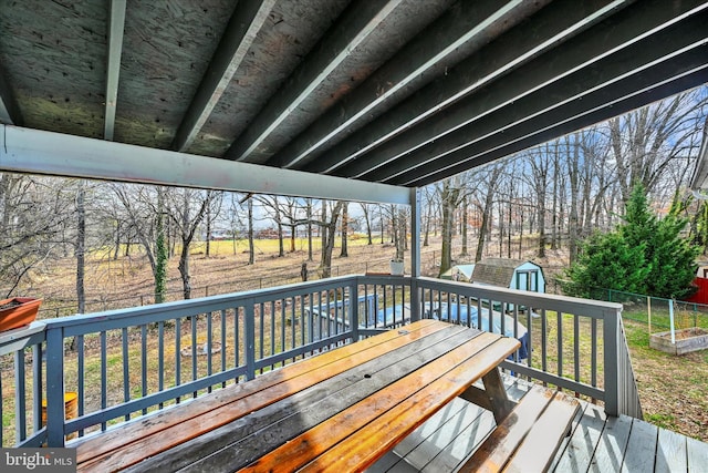 wooden terrace featuring outdoor dining area, a storage unit, an outbuilding, and fence