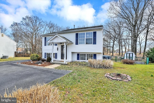 view of front of property featuring central AC unit, fence, a front lawn, an outdoor structure, and a storage shed