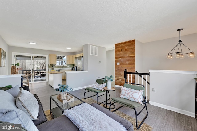 living room featuring wood finished floors, baseboards, visible vents, an inviting chandelier, and a textured ceiling