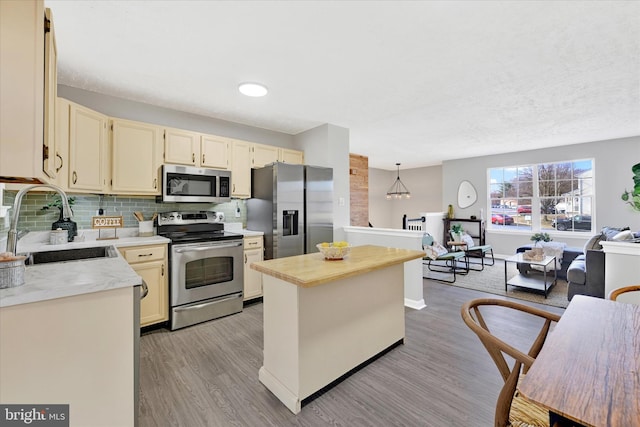 kitchen featuring light wood-type flooring, a sink, appliances with stainless steel finishes, tasteful backsplash, and a center island