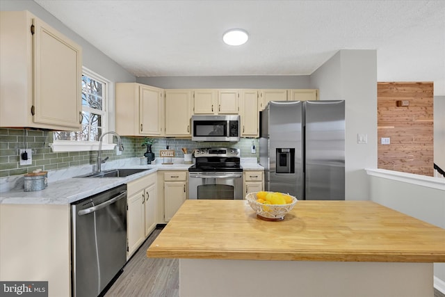 kitchen featuring a sink, butcher block countertops, stainless steel appliances, cream cabinets, and backsplash