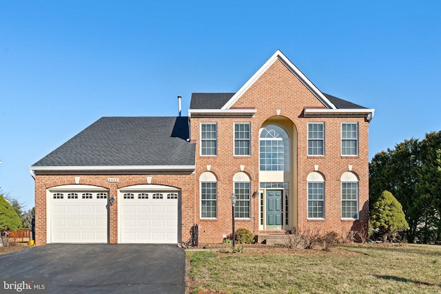 colonial inspired home with aphalt driveway, a front yard, brick siding, and an attached garage