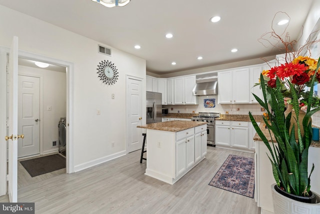 kitchen featuring visible vents, a kitchen island, appliances with stainless steel finishes, white cabinets, and wall chimney range hood