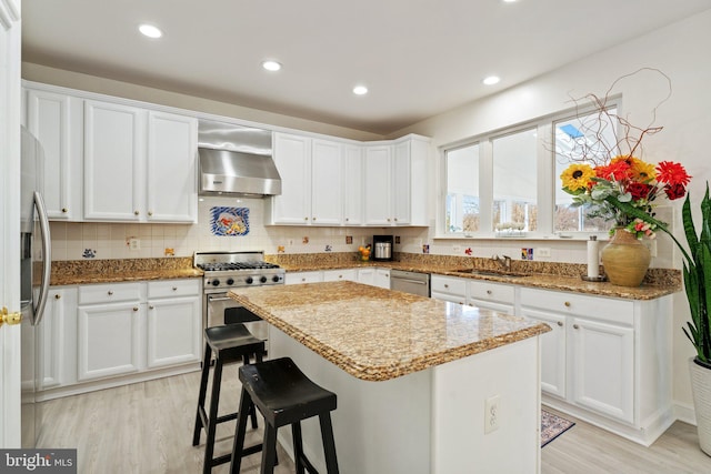 kitchen featuring a sink, a center island, white cabinetry, stainless steel appliances, and wall chimney range hood