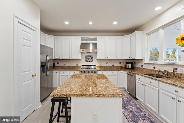 kitchen featuring a sink, stainless steel appliances, white cabinetry, wall chimney exhaust hood, and backsplash