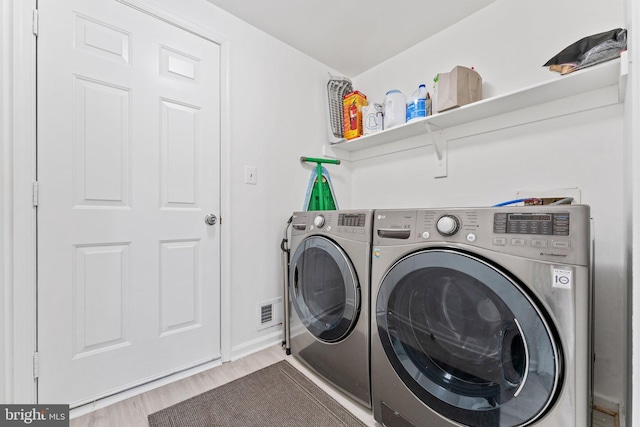 clothes washing area with washer and clothes dryer, laundry area, visible vents, and wood finished floors