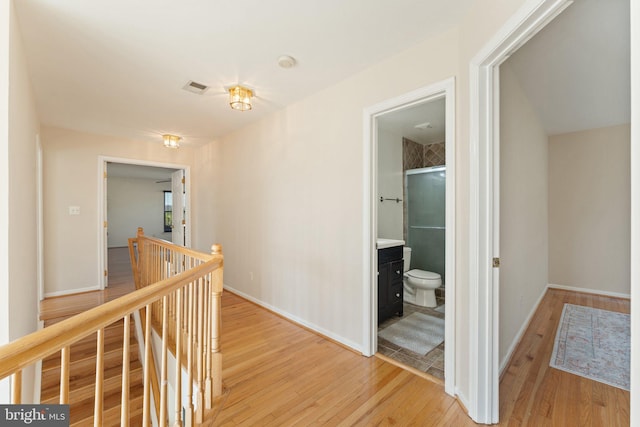 hall featuring an upstairs landing, visible vents, light wood-style flooring, and baseboards