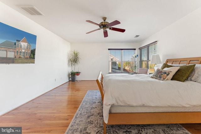 bedroom with a ceiling fan, wood finished floors, visible vents, and baseboards