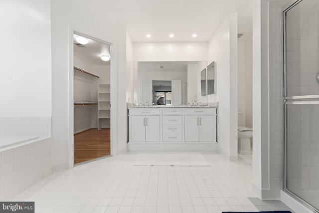 bathroom featuring double vanity, a sink, tile patterned flooring, a shower stall, and a walk in closet