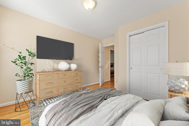 bedroom featuring light wood-type flooring, baseboards, and a closet