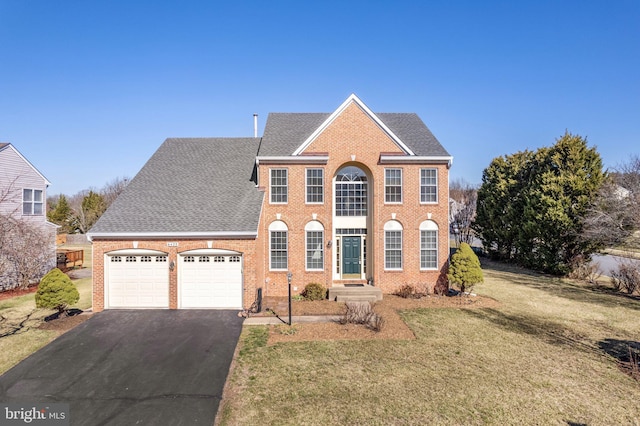 colonial house with driveway, roof with shingles, a front lawn, a garage, and brick siding