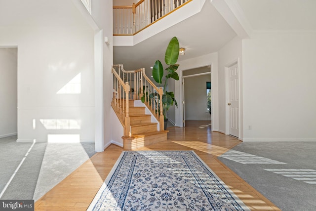 entrance foyer featuring baseboards, stairway, ornamental molding, a towering ceiling, and wood finished floors