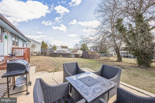 view of patio with grilling area, a shed, outdoor dining area, a fenced backyard, and an outbuilding