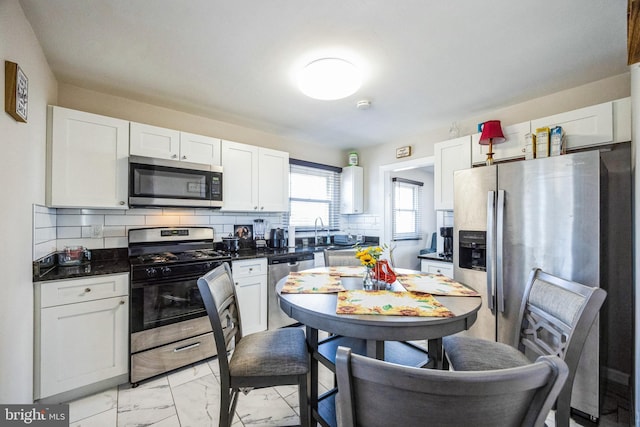 kitchen with tasteful backsplash, appliances with stainless steel finishes, marble finish floor, white cabinetry, and a sink