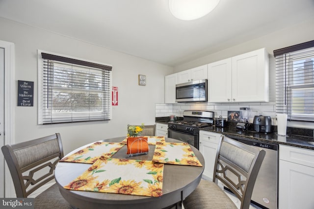 kitchen featuring stainless steel appliances, dark stone counters, backsplash, and white cabinetry