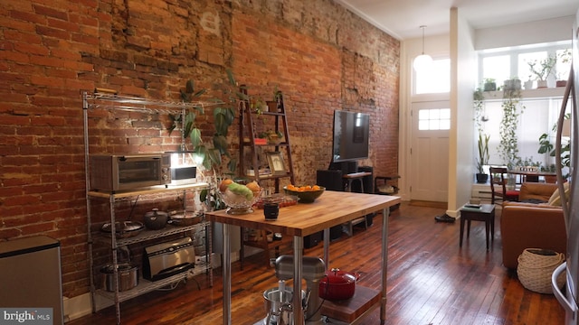 living area with wood-type flooring, brick wall, and a towering ceiling