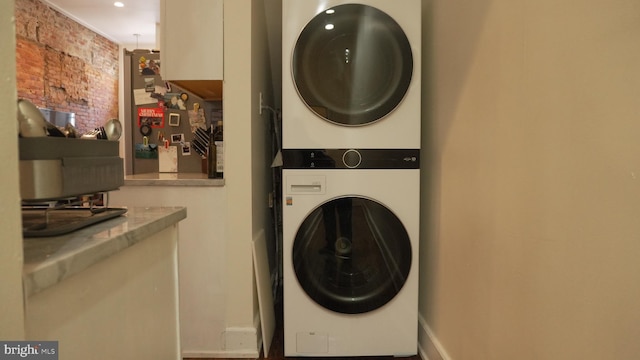 laundry area featuring brick wall, laundry area, and stacked washer / dryer