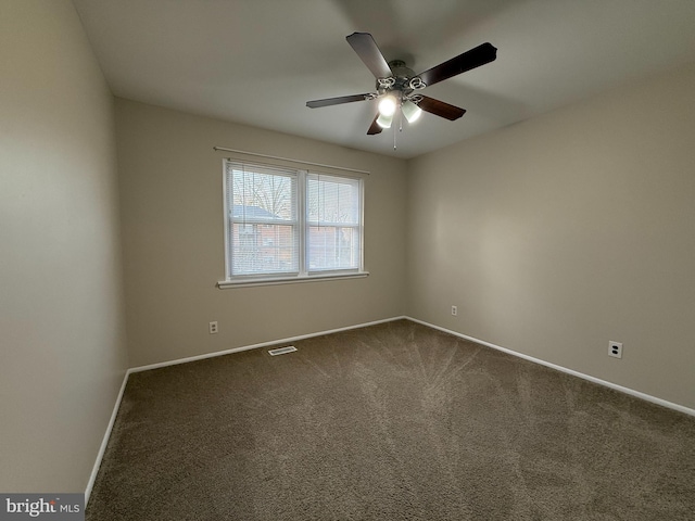 spare room with dark colored carpet, visible vents, baseboards, and a ceiling fan