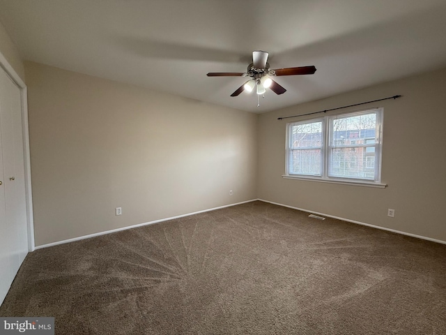 spare room with visible vents, baseboards, ceiling fan, and dark colored carpet