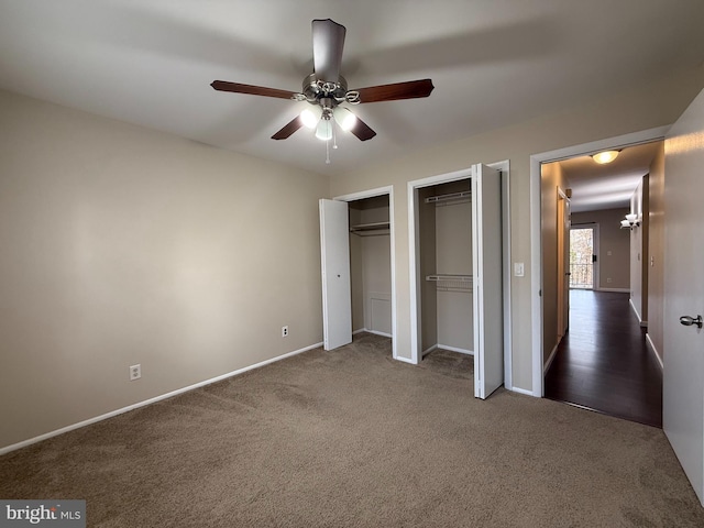 unfurnished bedroom featuring carpet flooring, two closets, baseboards, and a ceiling fan