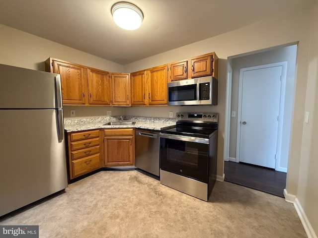 kitchen featuring brown cabinetry, stainless steel appliances, baseboards, and a sink