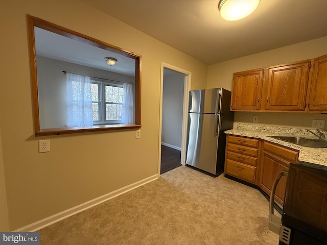 kitchen featuring a sink, light carpet, freestanding refrigerator, brown cabinetry, and range