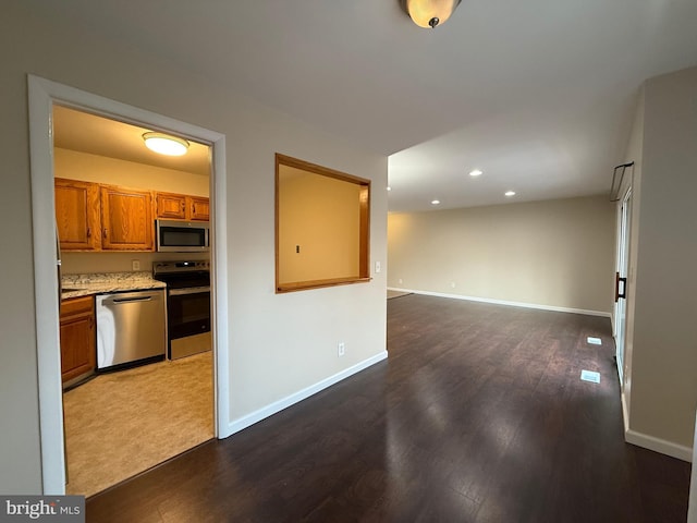 kitchen featuring brown cabinets, dark wood-type flooring, open floor plan, stainless steel appliances, and baseboards