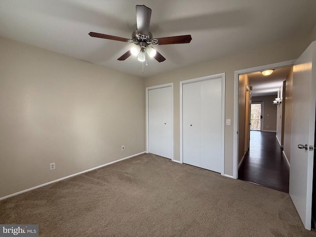 unfurnished bedroom with dark colored carpet, baseboards, two closets, and ceiling fan