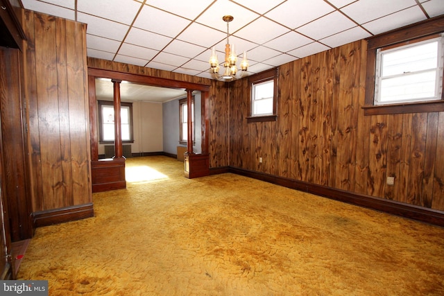 empty room with a paneled ceiling, plenty of natural light, and wooden walls