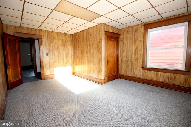 unfurnished room featuring wooden walls, a paneled ceiling, baseboards, and carpet floors