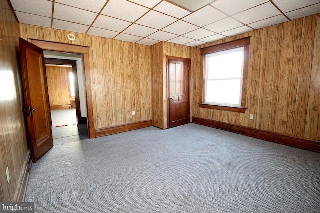 carpeted spare room featuring a drop ceiling, wood walls, and baseboards