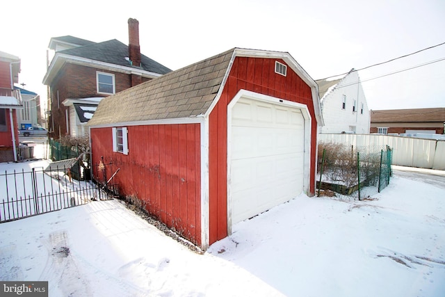 snow covered garage featuring a detached garage and fence