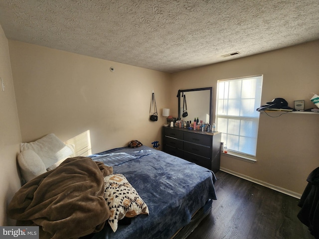 bedroom featuring visible vents, baseboards, a textured ceiling, and wood finished floors