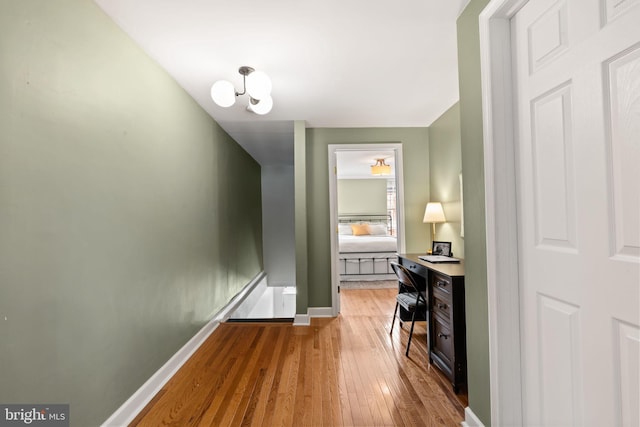 hallway with light wood-style flooring, a notable chandelier, and baseboards