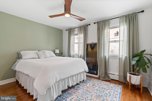 bedroom featuring a baseboard radiator, baseboards, wood finished floors, and a ceiling fan