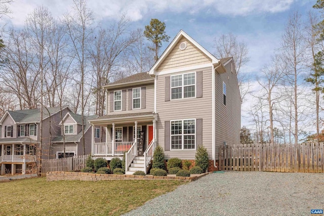 traditional-style home featuring driveway, a porch, a front yard, and fence