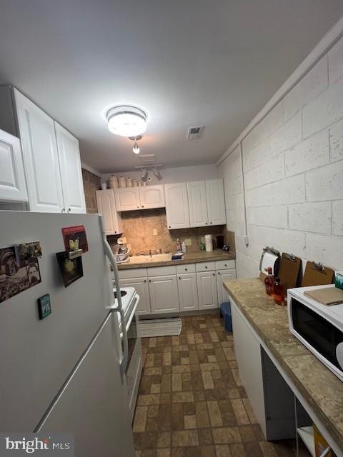 kitchen with white appliances, concrete block wall, decorative backsplash, light countertops, and white cabinetry