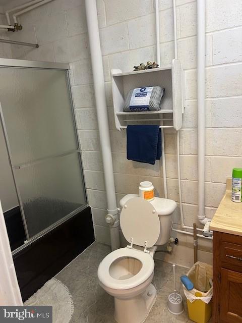 full bathroom featuring a shower with door, concrete block wall, toilet, and vanity