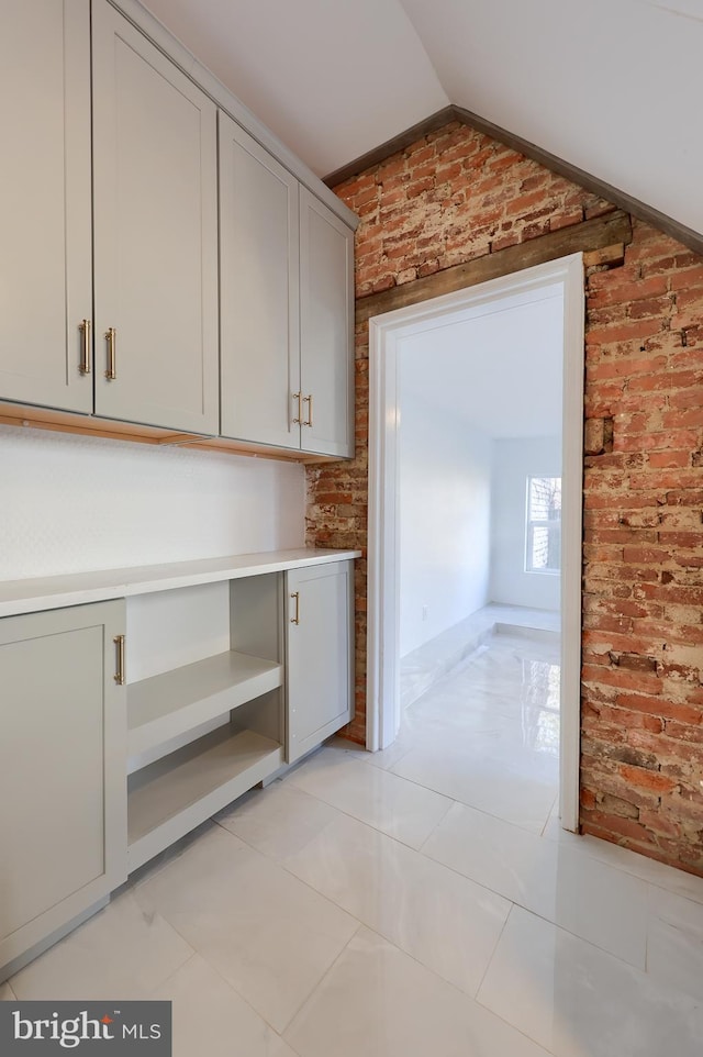 interior space with gray cabinets, brick wall, light countertops, and vaulted ceiling