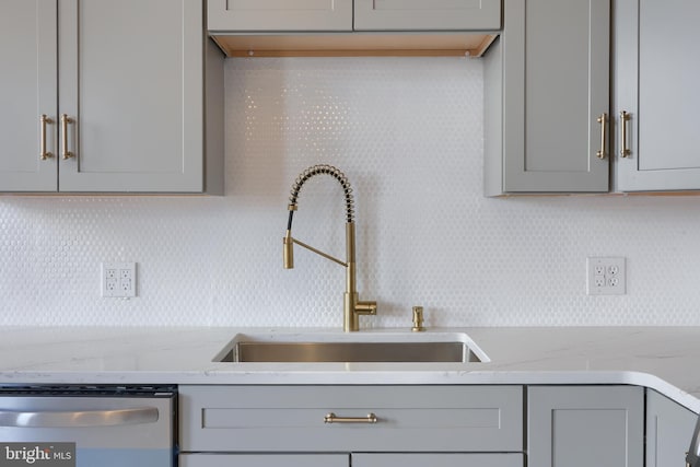 kitchen featuring gray cabinets, a sink, tasteful backsplash, stainless steel dishwasher, and light stone countertops