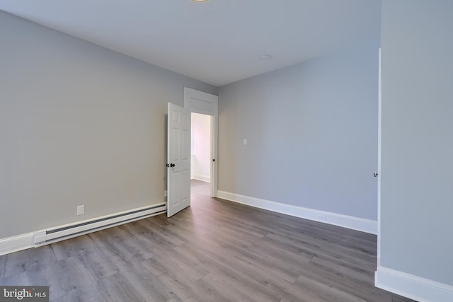 empty room featuring a baseboard radiator, baseboards, and wood finished floors