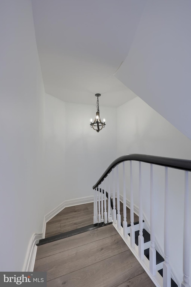 staircase featuring a notable chandelier, baseboards, and wood finished floors